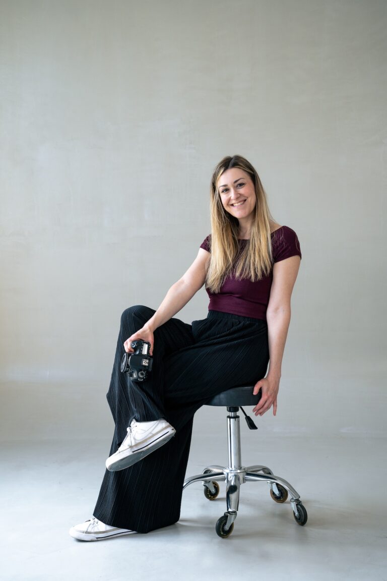 Videografin Theresa Klingohr lächelt auf Stuhl mit Kamera in der Hand während Content Produktion.